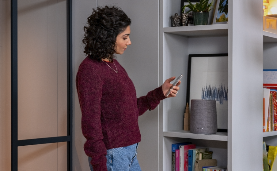 Een speaker op een kast, met een gebruiker die via smartphone muziek afspeelt